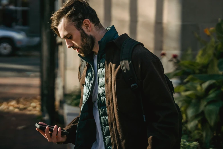 a man with a beard looking at his cell phone, trending on pexels, happening, brown jacket, avatar image, walking down, owen gent