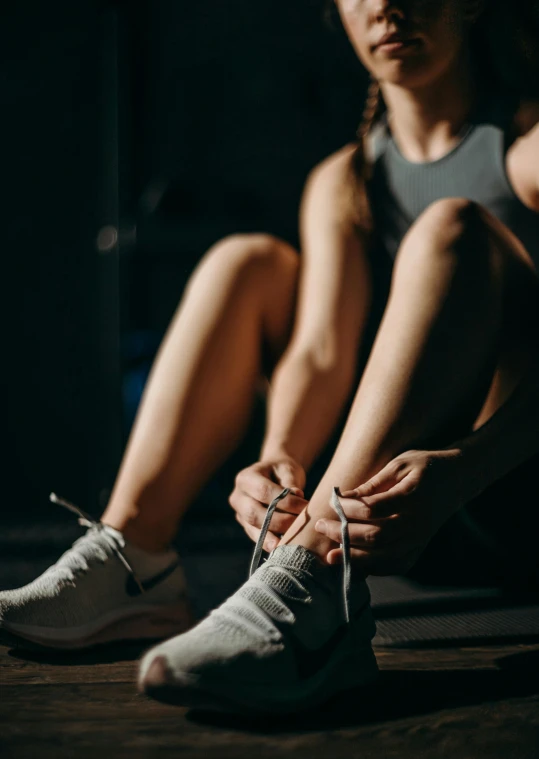 a woman tying up her shoes in the dark, trending on pexels, in a gym, avatar image