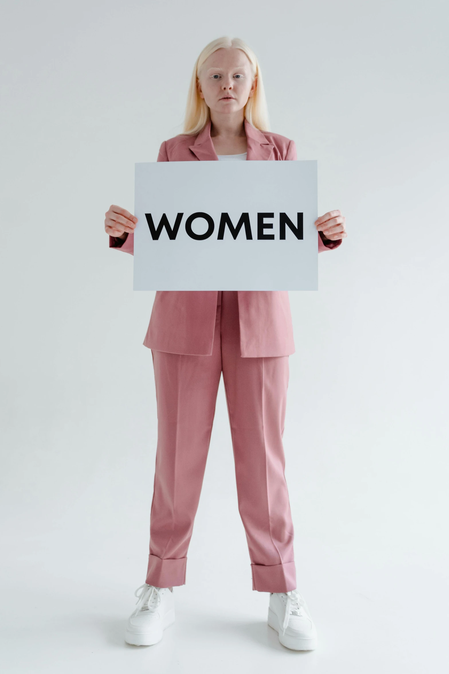 a woman holding a sign that says women, trending on pexels, wearing a light - pink suit, on a gray background, pale woman, female forms