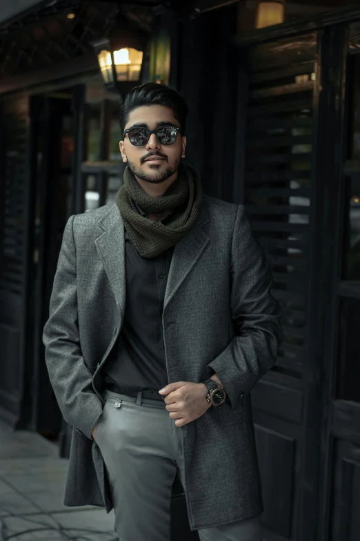 a man standing on a sidewalk in front of a building, inspired by Ismail Acar, trending on pexels, grey turtleneck coat, sunglasses and a scarf, zayn malik, formal attire