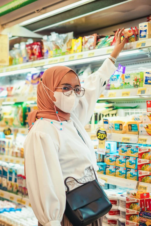 a woman wearing a face mask in a grocery store, by Julia Pishtar, pexels contest winner, white hijab, photo of young woman, square, malaysian