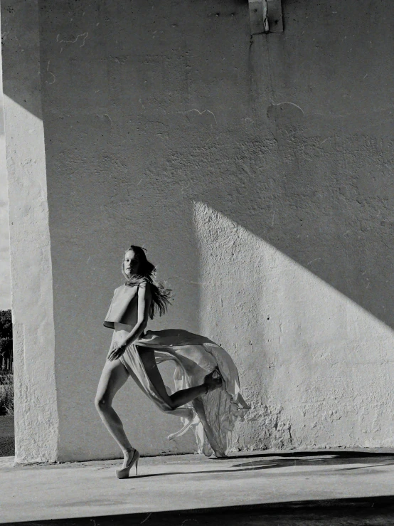 a woman walking down a sidewalk next to a building, inspired by Max Dupain, tumblr, dancing gracefully, sun overhead, photo from vogue magazine, waiting behind a wall
