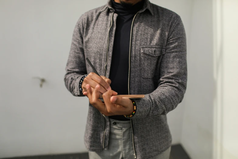 a man standing in a room holding a cell phone, an album cover, pexels contest winner, academic art, wearing two silver bracelets, pen and paper, wearing a turtleneck and jacket, wearing a dark blue polo shirt