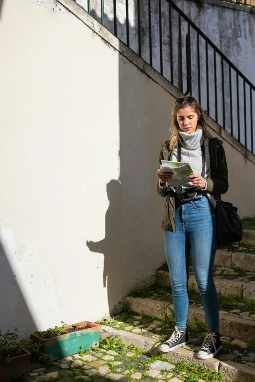 a woman standing on the steps of a building, reading a book, travel guide, wearing jeans, high shadow
