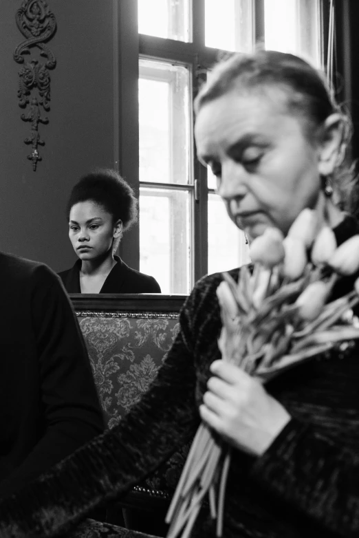 a woman sitting on a couch holding a bunch of flowers, a black and white photo, inspired by Carrie Mae Weems, flickr, renaissance, three women, walk in a funeral procession, looking threatening, filmstill