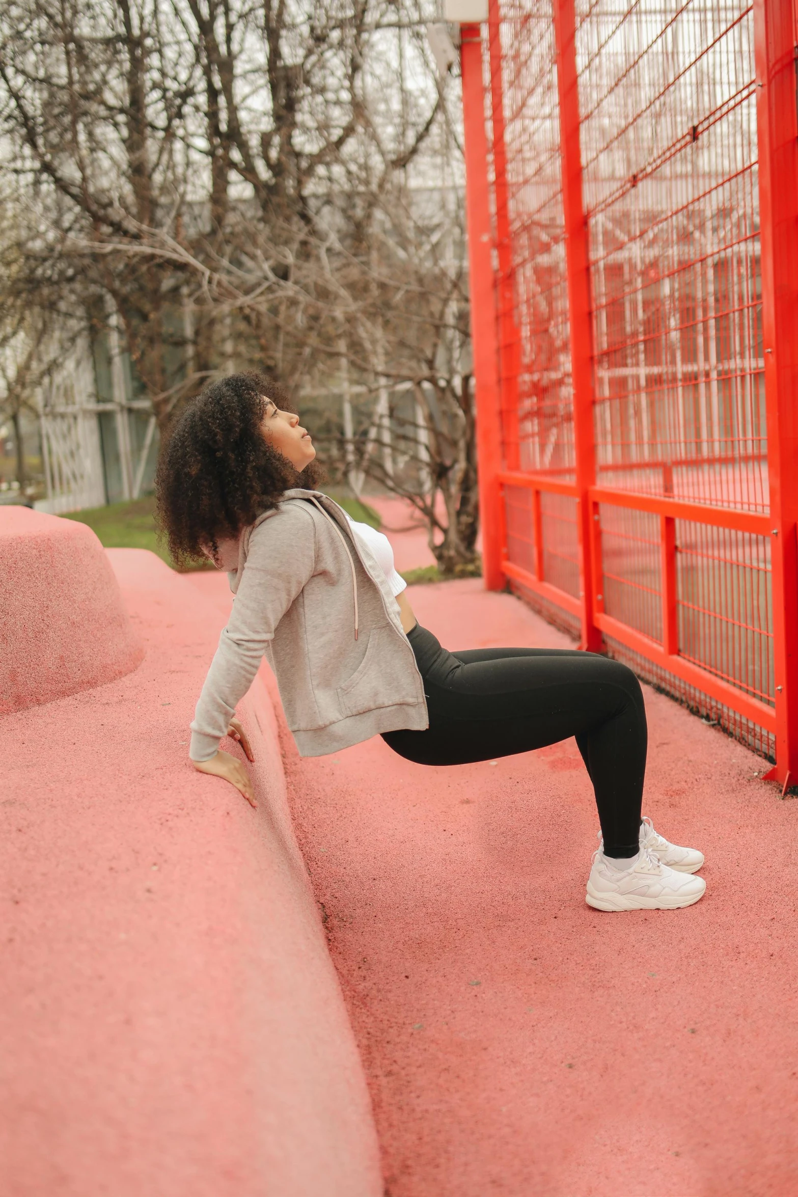 a woman sitting on a bench in front of a red fence, stretching to walls, profile image, playground, black young woman
