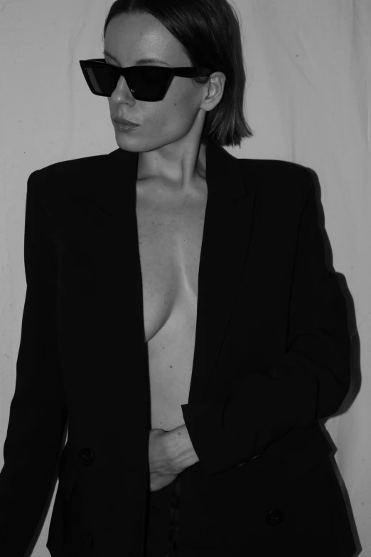 a black and white photo of a woman in a suit and sunglasses, inspired by Helmut Newton, unsplash, minimalism, breasts covered and sfw, kim kardashian, jacket over bare torso, kirsi salonen