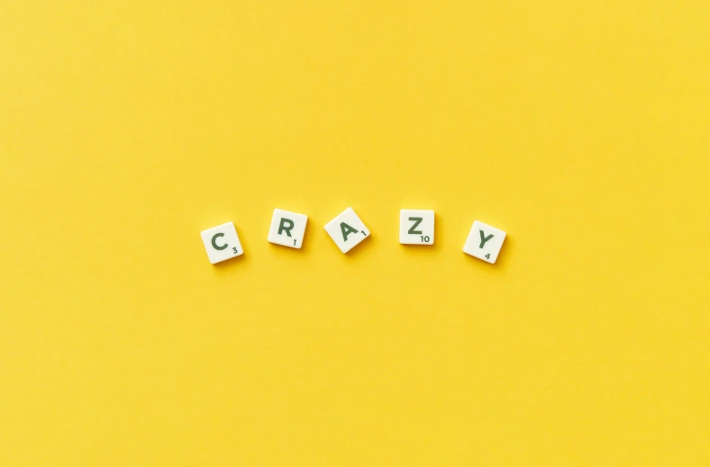 the word crazy spelled in scrabbles on a yellow background, by Caro Niederer, letterism, nootropic stimulant, 🦩🪐🐞👩🏻🦳, minimalistic background, scary stories