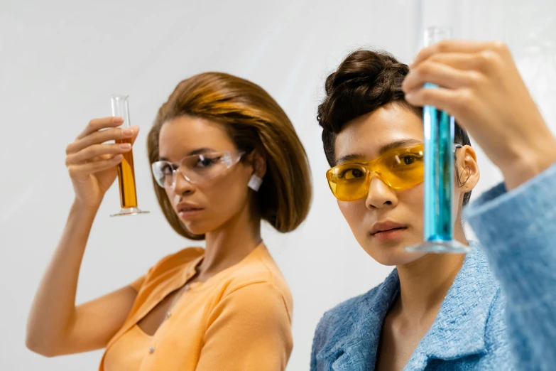 a couple of women standing next to each other holding test tubes, trending on pexels, fantastic realism, yellow carrera glasses, tan complexion, charli bowater and artgeem, industrial party