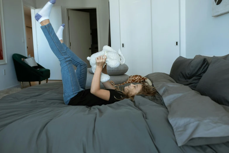 a woman laying on top of a bed holding a stuffed animal, inspired by Elsa Bleda, pexels contest winner, full body angle, flat grey color, teenager hangout spot, playing