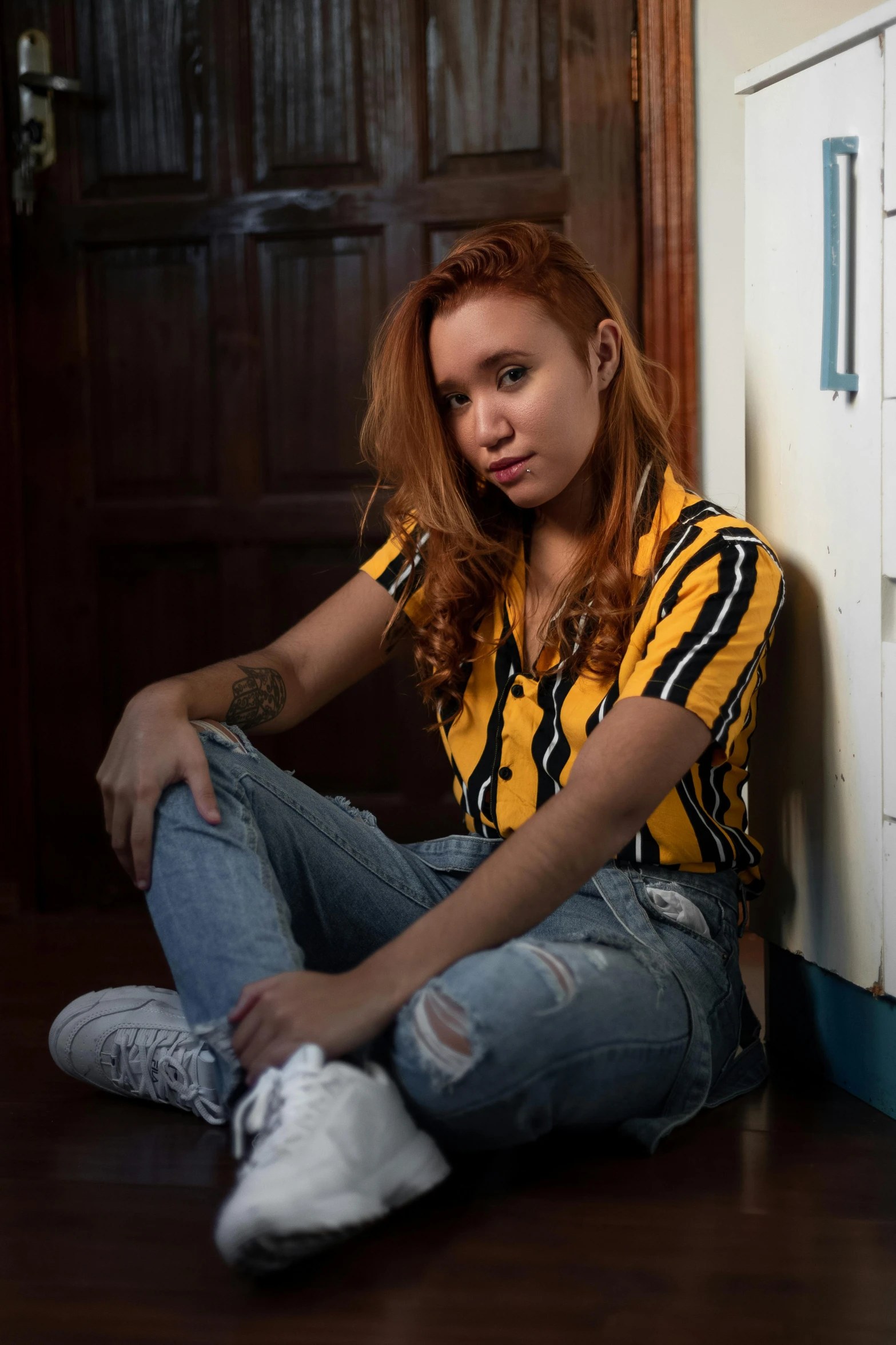 a woman sitting on the floor in front of a door, a portrait, inspired by Jorge Jacinto, trending on pexels, hyperrealism, ginger hair, black and yellow, kawaii shirt and jeans, tattooed