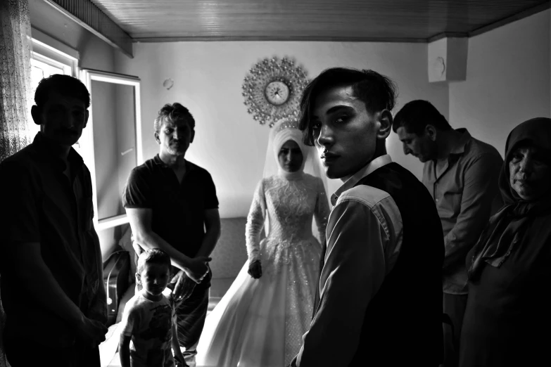 a group of people standing in a room, a black and white photo, by Ibrahim Kodra, pexels contest winner, hurufiyya, wearing a wedding dress, a boy, an ultra realistic, drag