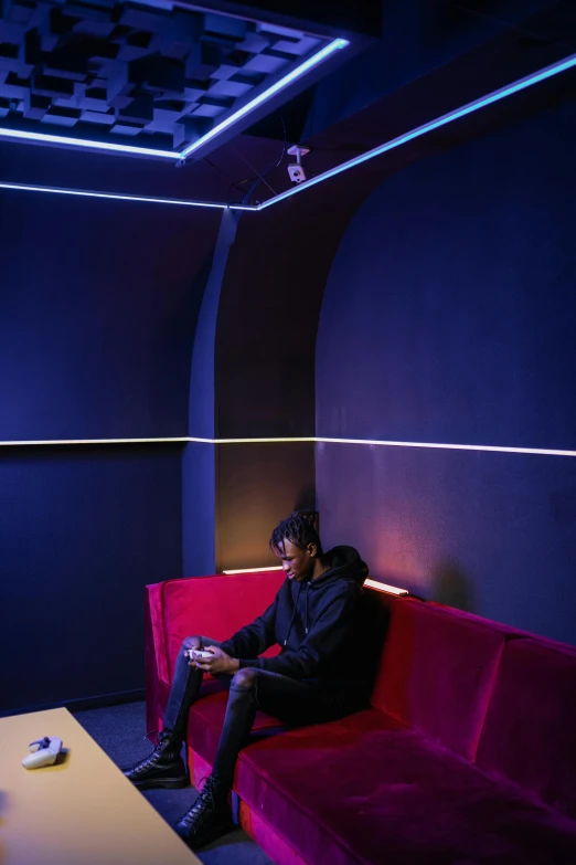 a man sitting on a red couch in a room, an album cover, inspired by Jean Tabaud, unsplash, light and space, sci-fi night club, rgb wall light, full body profile camera shot, contemplating