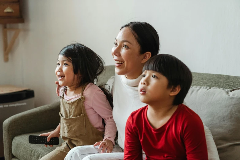 a woman and two children sitting on a couch, a cartoon, pexels contest winner, incoherents, asian female, watching tv, high quality photo, looking upward