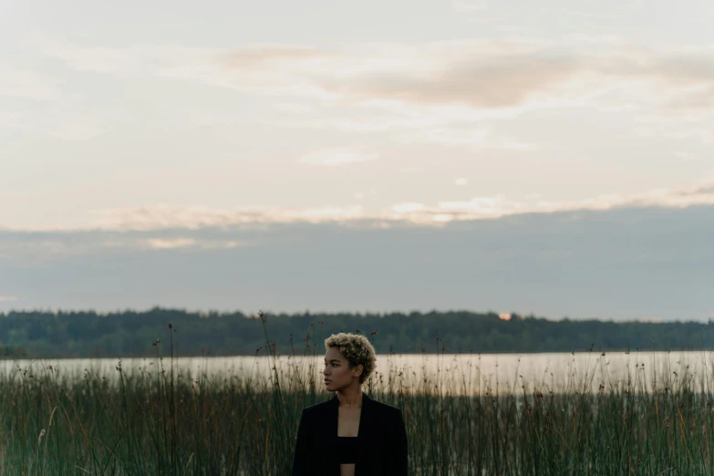 a woman standing in front of a body of water, an album cover, unsplash, spring evening, androgynous, aleksander rostov, ashteroth