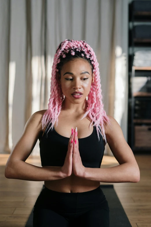 a woman sitting in a yoga pose on a yoga mat, by Matija Jama, trending on pexels, renaissance, pink hair covered with hairpins, prayer hands, african american young woman, long braided hair on top of head