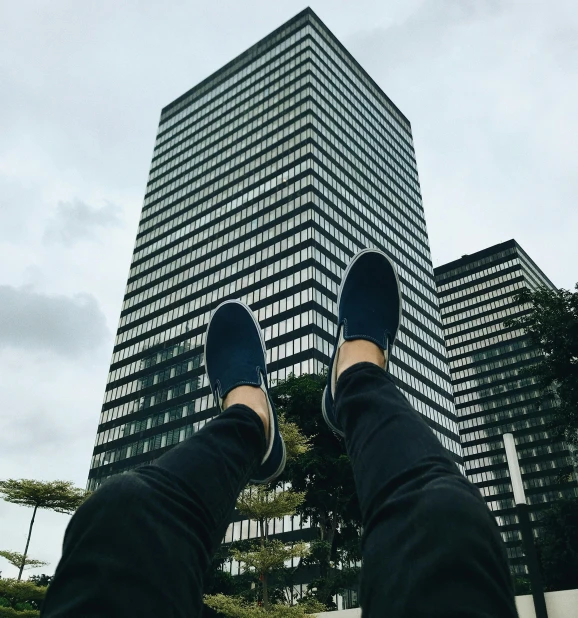 a person standing in front of a tall building, pexels contest winner, blue shoes, relaxing, kickflip, low quality photo
