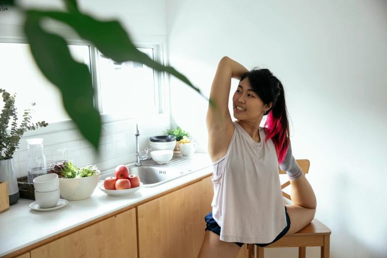 a woman sitting on a stool in a kitchen, by Jang Seung-eop, pexels contest winner, happening, sport bra and shirt, stretch, afternoon hangout, upper body image