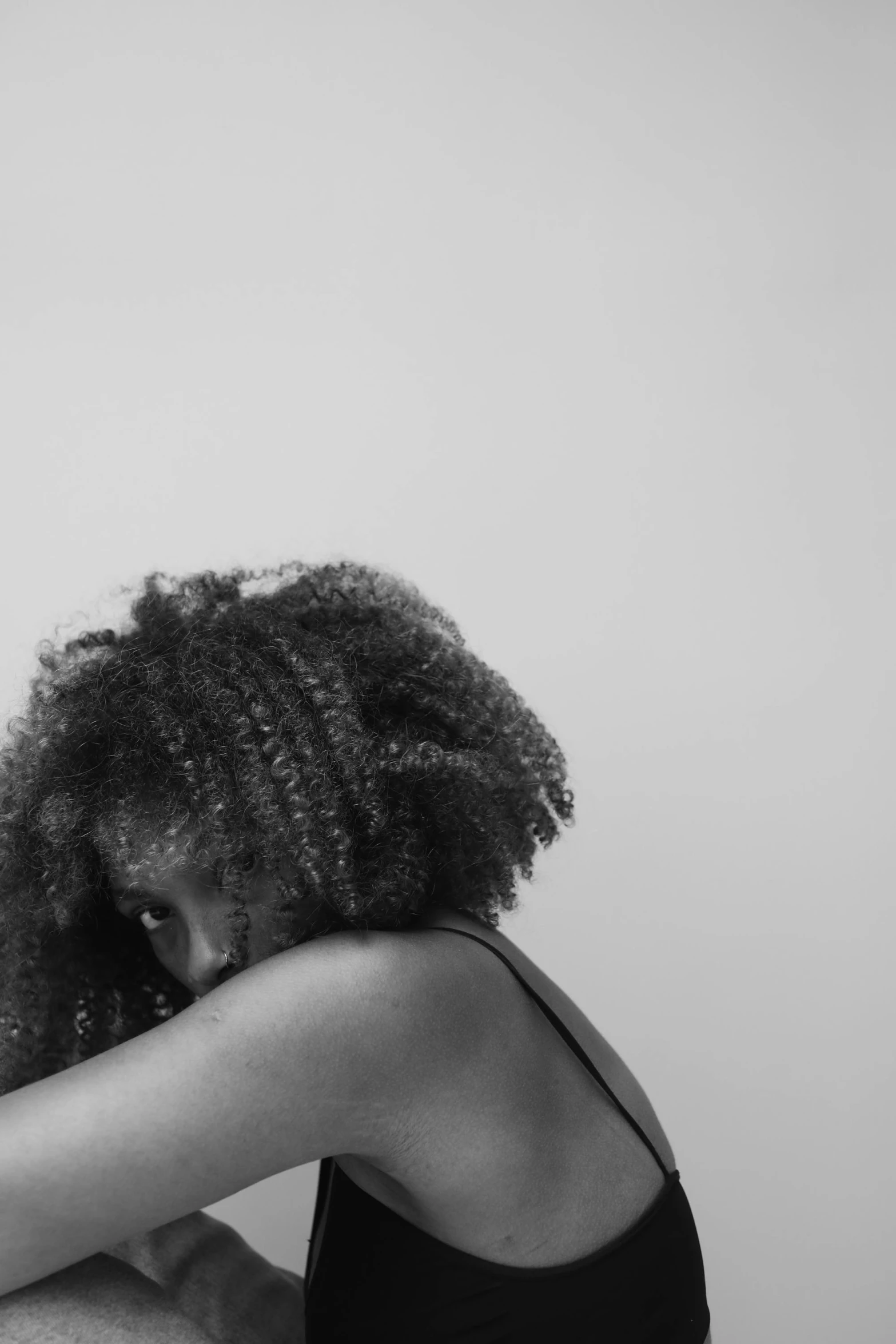 a black and white photo of a woman sitting on a bed, inspired by Carrie Mae Weems, unsplash, hair over face, embraced, hunched over, curls