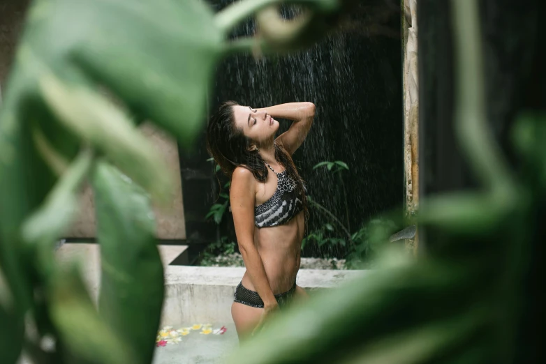 a woman in a bikini standing in a pool of water, unsplash, lush foliage, raining outside, well built, alana fletcher