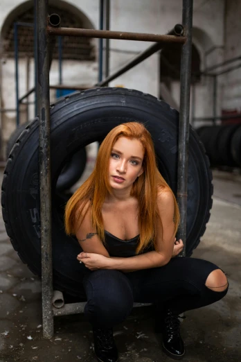 a woman sitting on a tire in a warehouse, a portrait, by Adam Marczyński, pexels contest winner, red hair and attractive features, in an arena pit, mechanic, headshot profile picture