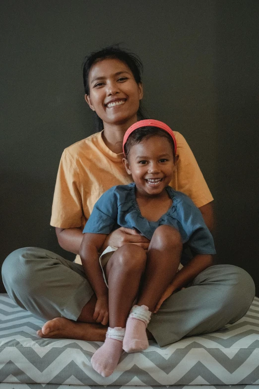 a woman and a child sitting on a bed, pexels contest winner, sumatraism, smiling with confidence, sitting on the floor, promo image, multiple stories