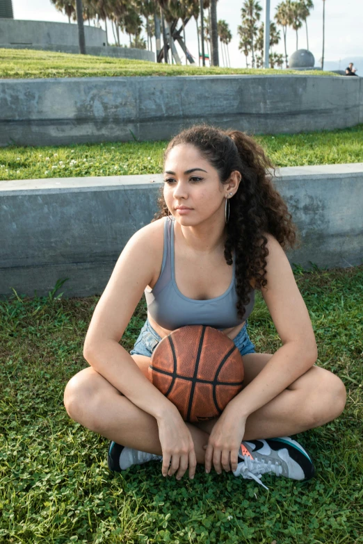 a woman sitting on the ground holding a basketball, latino features, teenager hangout spot, curls, 2019 trending photo