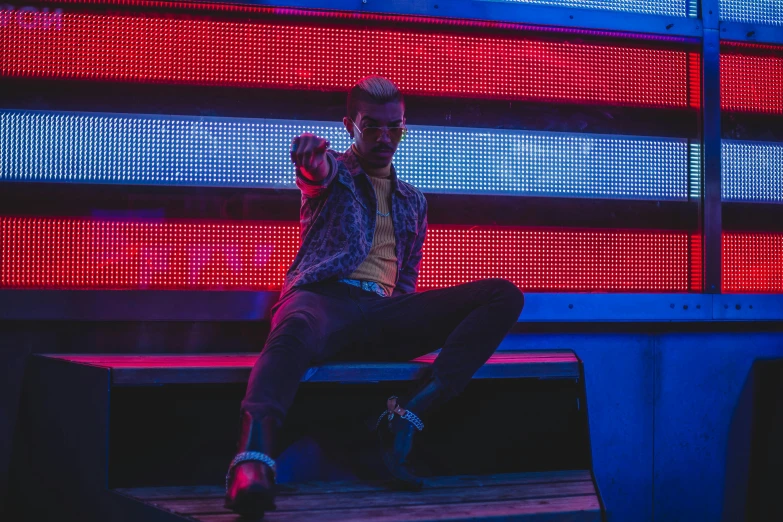 a man sitting on a bench in front of an american flag, an album cover, pexels contest winner, fashion neon light, badass pose, blue and red lights, concert