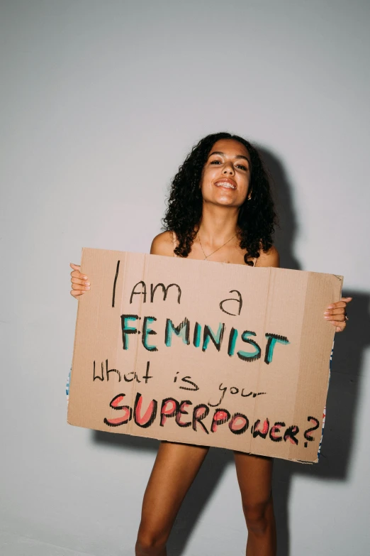 a woman holding a sign that says i am a feminist what's your superpower?, an album cover, trending on pexels, feminist art, essence, body portrait, brown, light skin