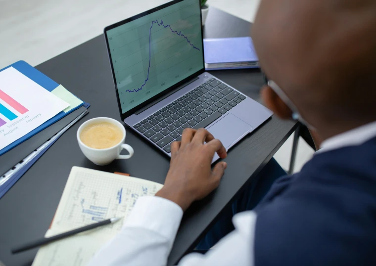 a man sitting at a desk using a laptop computer, pexels, analytical art, graphs, afro tech, official screenshot, bending down slightly