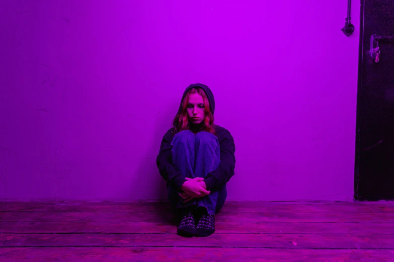 a woman sitting on the floor in front of a purple wall, inspired by Elsa Bleda, pexels, antipodeans, small red lights, portrait of depressed teen, sydney sweeney, black light