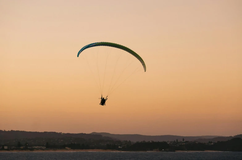 a person flying a parachute over a body of water, by Peter Churcher, pexels contest winner, hurufiyya, in a sunset haze, manly, riding in the sky, sunset panorama