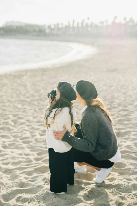 a couple of women sitting on top of a sandy beach, unsplash contest winner, romanticism, taking a picture, petite girl, warmly lit, grainy