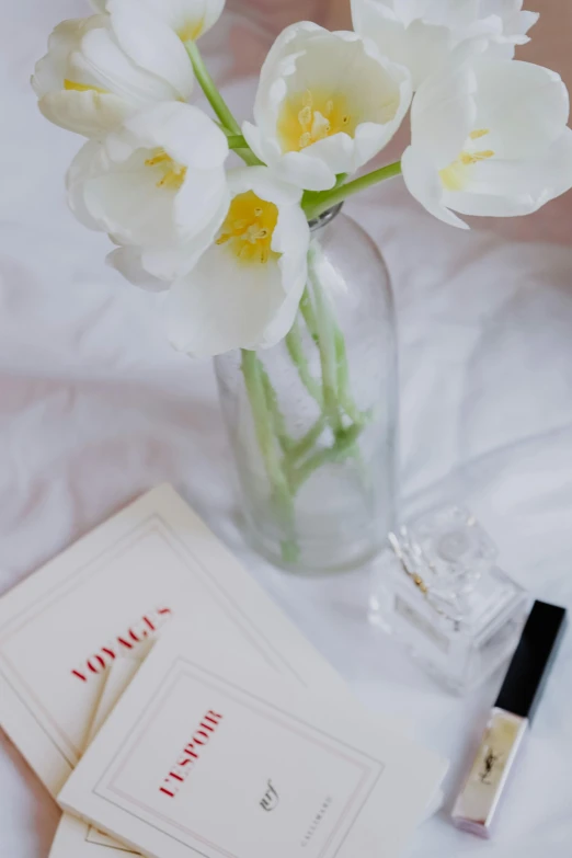 a vase filled with white flowers on top of a bed, with notes, perfume, understated aesthetic, set photograph