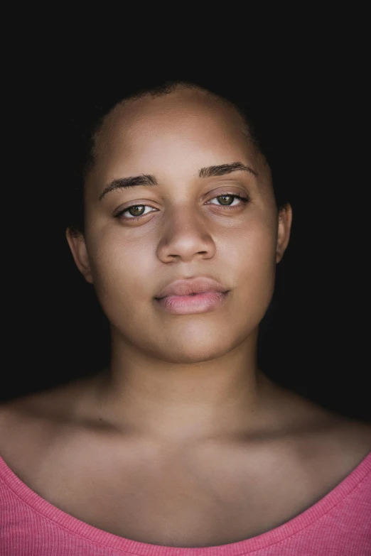 a close up of a person wearing a pink shirt, by Lily Delissa Joseph, flickr, visual art, spotlight in middle of face, mixed-race woman, somber expression, without makeup