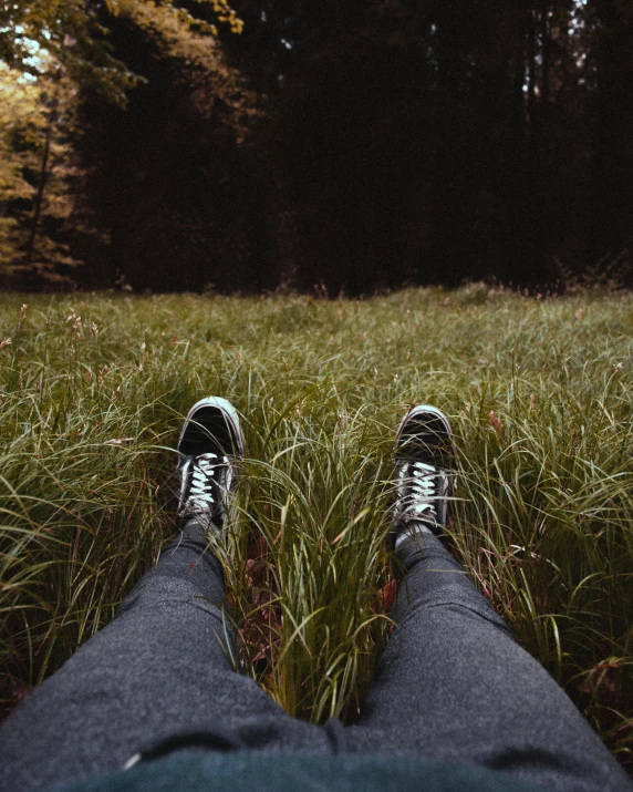 a person sitting in a field of tall grass, wearing white sneakers, ((forest)), sitting across the room, trending photo