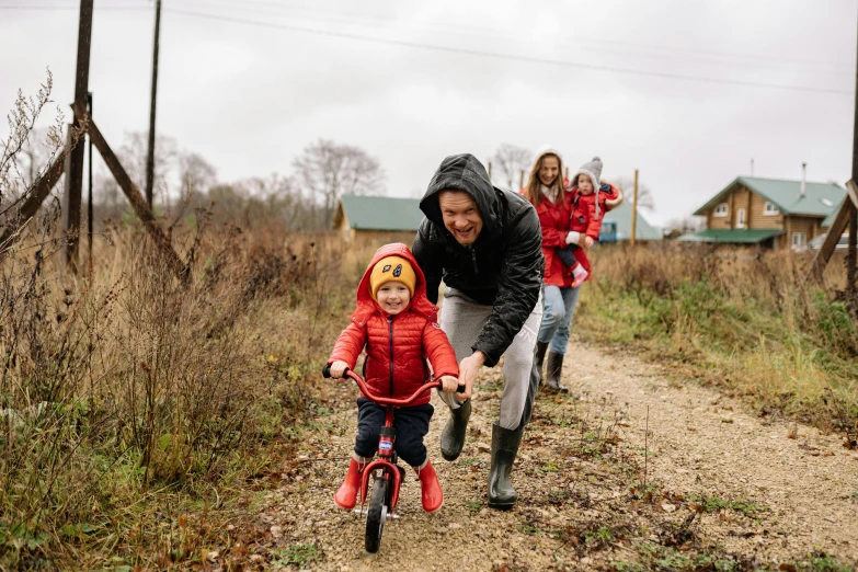 a man teaching a child how to ride a bike, by Julia Pishtar, pexels, wearing a scarlet hoodie, on a farm, happy family, 5k