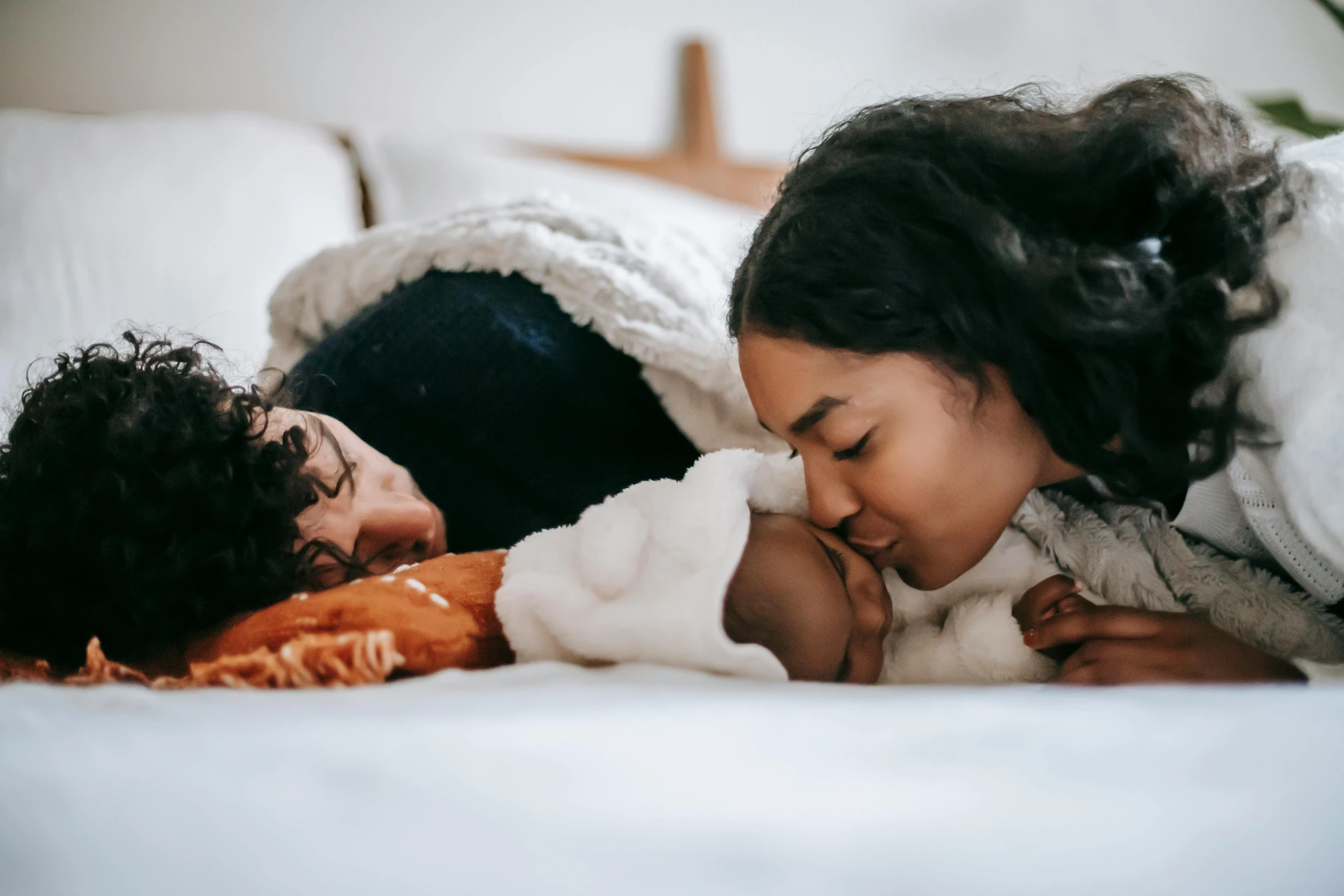 a woman laying on top of a bed next to a baby, pexels contest winner, hurufiyya, couple kissing, manuka, profile image, woman holding another woman