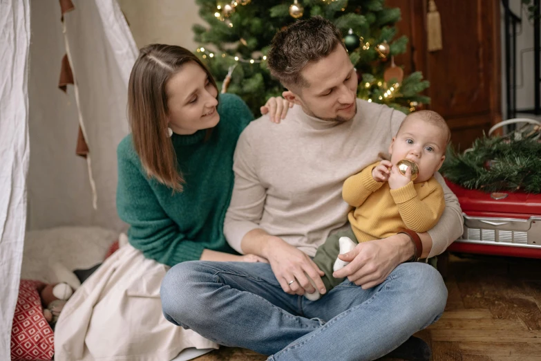 a man and woman holding a baby in front of a christmas tree, pexels, handsome man, avatar image, 1 5 6 6, indoor picture
