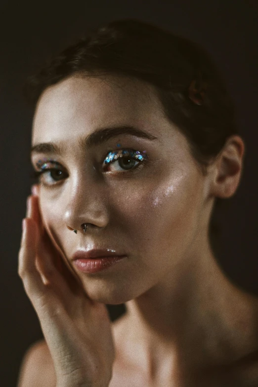 a woman with blue eyes holding her hand to her face, a hyperrealistic painting, inspired by Elsa Bleda, trending on pexels, li bingbing, glossy flecks of iridescence, with a black background, cyberpunk pincushion lens effect