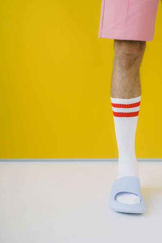 a man in pink shorts and white socks standing in front of a yellow wall, red stripe, wearing kneesocks, getty images, wearing white tights