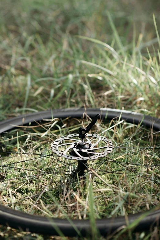 a close up of a bicycle tire in the grass, an album cover, by Mathias Kollros, land art, black rims, gears, lightweight, b - roll