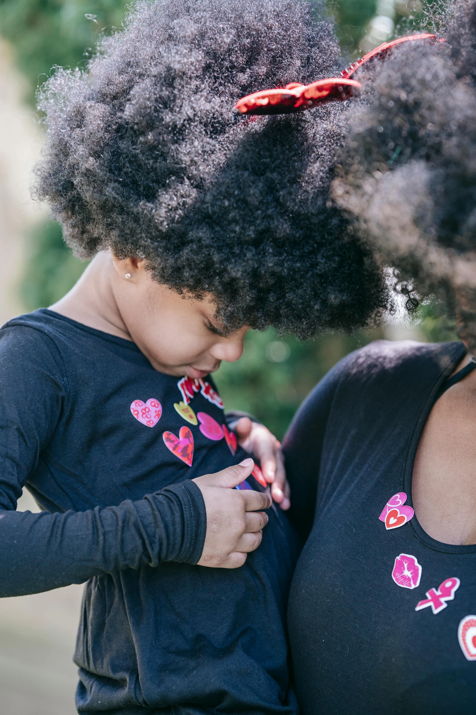 a woman holding a small child in her arms, by Winona Nelson, pexels contest winner, process art, embroidered shirt, hearts, with afro, casual black clothing