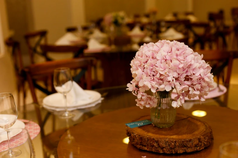 a vase filled with pink flowers sitting on top of a wooden table, restaurant, ameera al taweel, hydrangea, accurate details