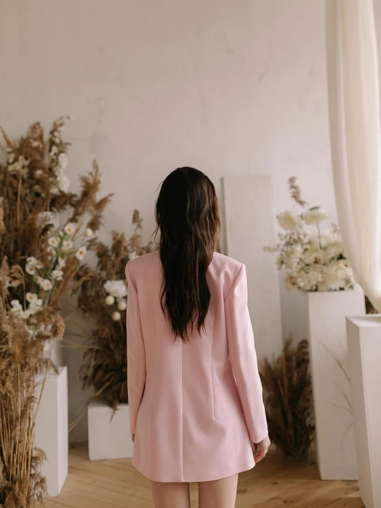 a woman standing in front of a vase of flowers, by Emma Andijewska, wearing a light - pink suit, back view. nuri iyem, bae suzy, back view »