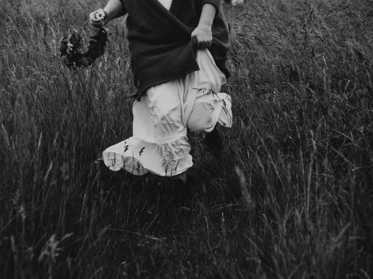 a black and white photo of a little girl in a field, by Emma Andijewska, unsplash, process art, carrying flowers, layered skirts, bare feet in grass, hunting