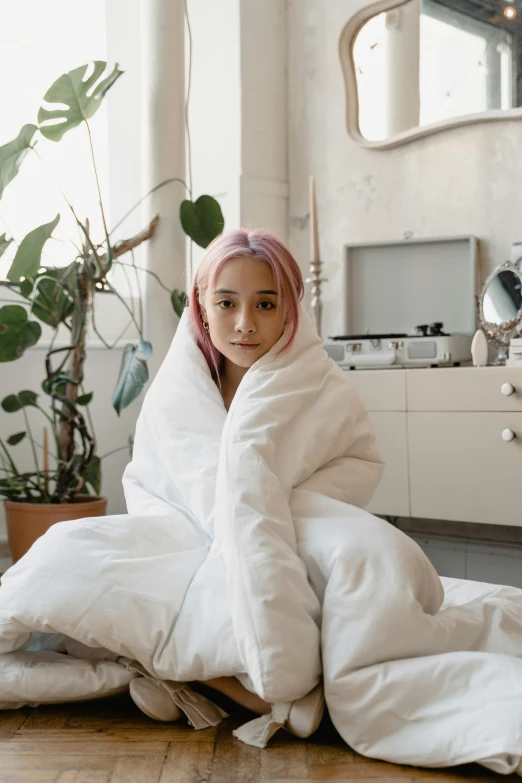 a woman sitting on the floor wrapped in a blanket, trending on unsplash, with pink hair, un made bed, asian descent, white coat