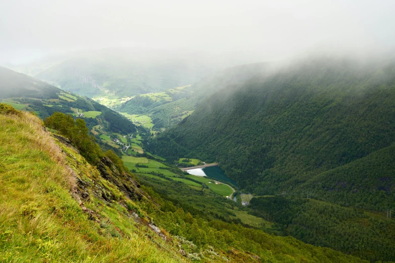 a man standing on top of a lush green hillside, inspired by Hallsteinn Sigurðsson, pexels contest winner, hurufiyya, rivers and lakes, low clouds after rain, youtube thumbnail, lush forest in valley below