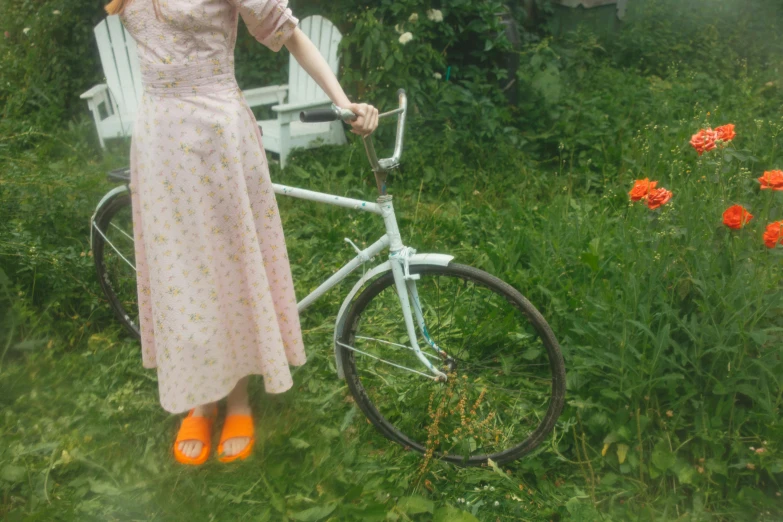 a woman standing next to a bicycle in a field, inspired by Elsa Beskow, pexels contest winner, white and orange, in the yard, transparent, legs visible