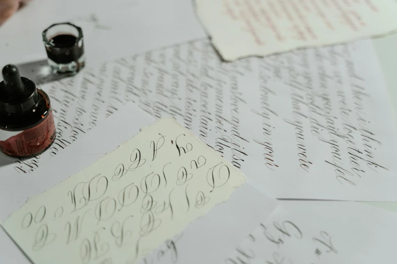 a table topped with lots of writing and a bottle of ink, by Emma Andijewska, pexels, letterism, silver，ivory, background image, 1759, schools